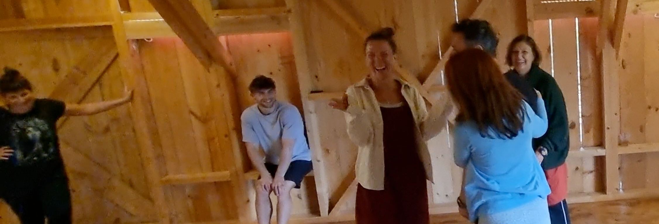 Un grupo de participantes del curso ríe en una sala de madera clara: una mujer en el centro se lleva una mano a la cara mientras los demás la miran.