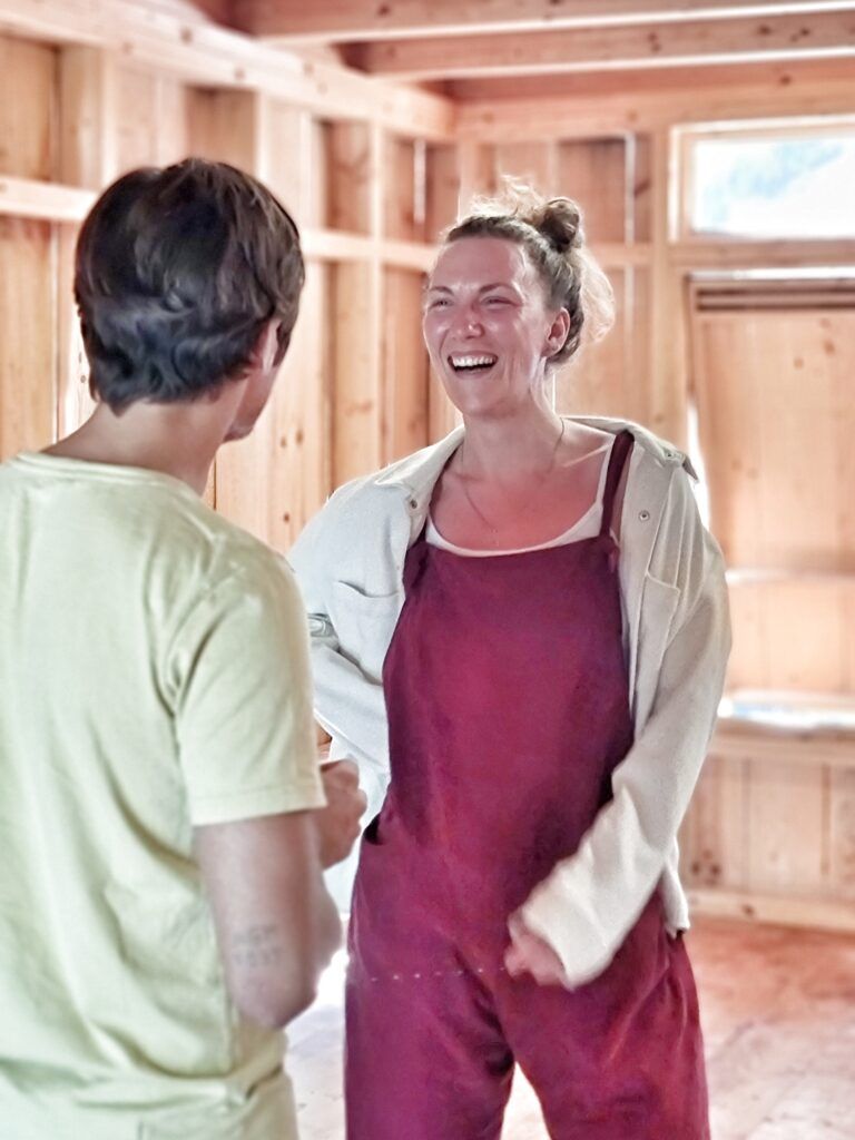 Una participante del curso, con peto rosa empolvado, ríe a carcajadas frente a otra persona, en una sala revestida de madera clara.